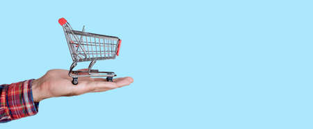 Supermarket trolley in hand on empty colored background. Online grocery shopping and selling conceptの写真素材