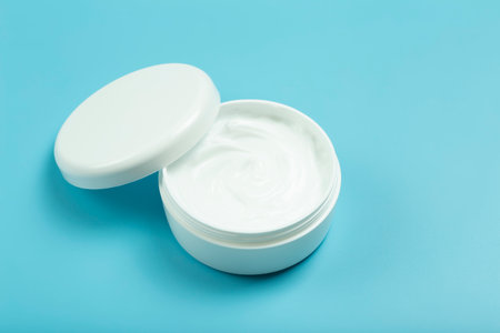 Cosmetic cream background. White cosmetic cream for skin and body in an open white jar on a colored blue empty background.の写真素材