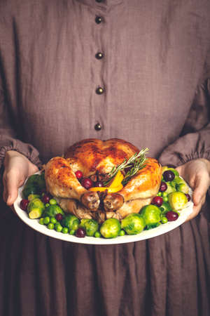 Thanksgiving turkey or chicken for a festive dinner. A plate of fried chicken in the hands of a woman in a classic American dress. Thanksgiving and autumn seasonal food concept.の写真素材