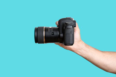 Hand with a camera. A hand holding a digital SLR camera on a clean blue background. high quality...