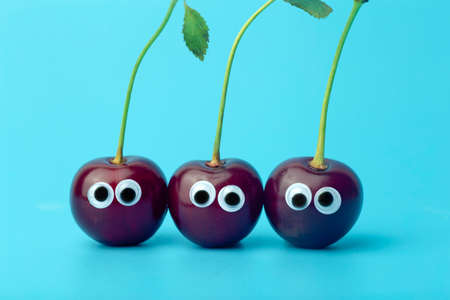 Cherry eyes on a blue background. Funny vegetables and fruits for children. Baby food concept, food face.の写真素材