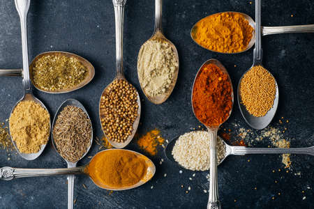 Spices in spoons background. Varieties of spices turmeric, pepper, chili, coriander, cinnamon and peppers for cooking. Culinary food concept.の写真素材