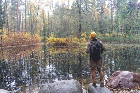 Traveler in the woods. A man with a backpack walks and trips on a track in a beautiful autumn forest and admires the lake and natural views. Traveling to nature in the forest aloneの写真素材