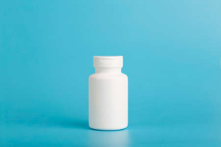 Jar of pills isolate. White plastic jar for medical pills, drugs and vitamins on a blank blue background.の写真素材