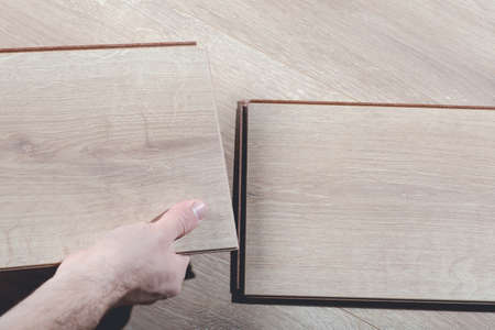 Installing laminate flooring in a room or office. Wooden parquet boards in the hands of a worker. Construction and decorative works for the finishing of housingの写真素材