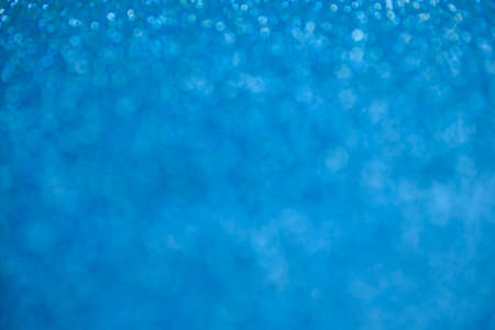 Glitter blue background. Texture foil and confetti bokeh, light of blue dust. Festive party Christmas and new years eve background.の写真素材