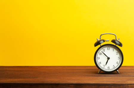 Vintage alarm clock on a yellow background. Black alarm clock showing morning time on the table. Time concept.の写真素材