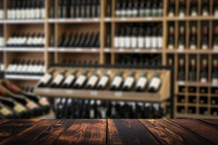 Wine wooden table background. Blurred wine shop with bottles on the counter.の写真素材