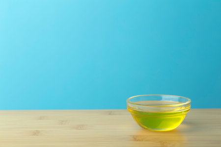 Oil in a glass bowl on a clean blue background. Cosmetic or food oil background. Copy spaceの写真素材