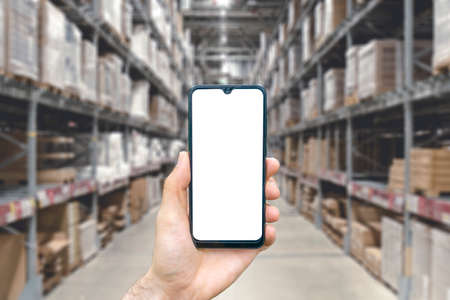 Warehouse with a hand holding an empty smartphone. Blurred industrial warehouse with goods and products. Logistics, business, delivery, services conceptの写真素材