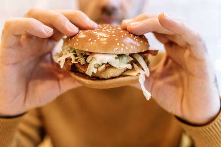 A man eats a burger with meat in a cafe. Fast food, junk food, fast carbs, obesity, overeating, stress concept.の写真素材