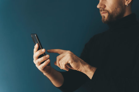 Using a smartphone by a young man on a blank background. Phone in hand while using the Internet,...