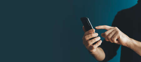 Using a smartphone by a young man on a blank background. Phone in hand while using the Internet, messenger, shopping, communication. Technology, applications, business concept.の写真素材
