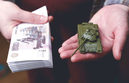 Russian rubles banknotes and toy tank in hands during the war in Ukraine. Inflation, sanctions and the fall of the Russian economy concept. Falling cash savings and budgetの写真素材