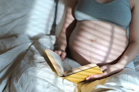 A pregnant woman reads a book and strokes her belly with a baby before childbirth while relaxing in...