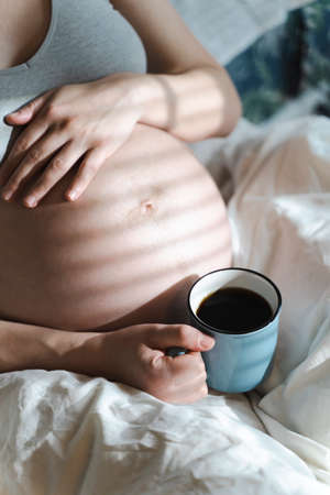 A pregnant woman holds a cup of coffee in her hands. Caffeine safety, myths about coffee during pregnancy conceptの写真素材