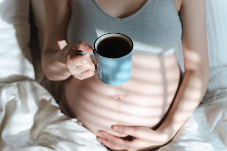 A pregnant woman holds a cup of coffee in her hands. Caffeine safety, myths about coffee during pregnancy conceptの写真素材