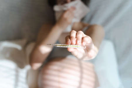 Pregnant woman during a cold and illness holds a thermometer with a high body temperature. Health during childbirth and pregnancyの写真素材