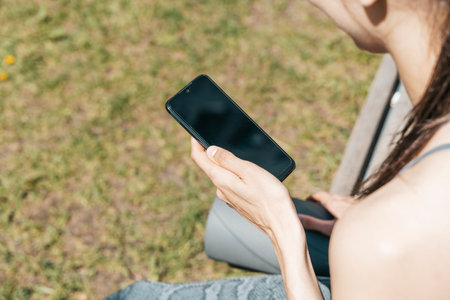 Sports girl using smartphone after yoga workout outdoors. Sports app, internet, technology, lifestyle concept.の写真素材