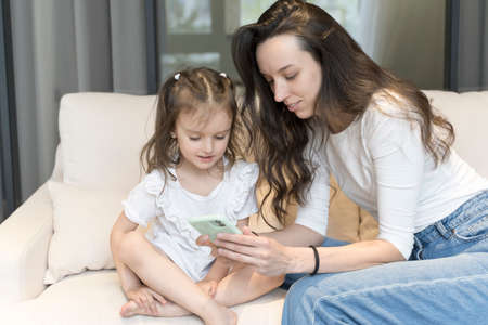 Mom and daughter use smartphone while playing and learning. Technology, internet and children. Parenthood, education, training, free time with children concept.の写真素材