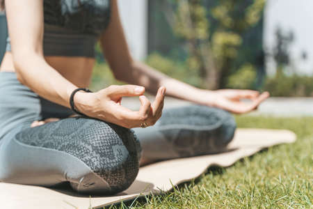 A woman meditates in the lotus position and relaxes in nature in the park in summer sunny weather. Yoga, mental health, relaxation, health concept.の写真素材