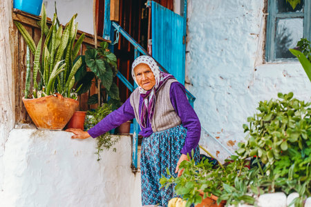 Kash, Turkey - November 28, 2022: Turkish old woman near her house with plants on Kas tourist street.のeditorial素材