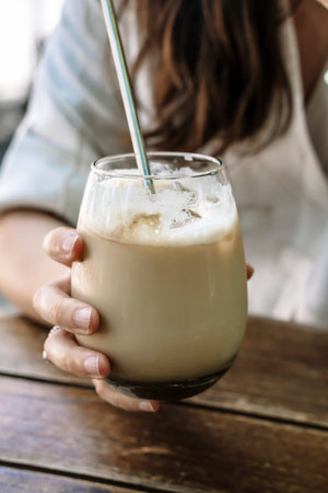 Ice latte in hand. A glass glass of cold coffee drink with milk in the hand of a girl in a summer...