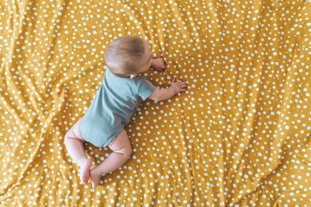 Cheerful baby lies on the bed in the childrens room. Caucasian baby smiles.