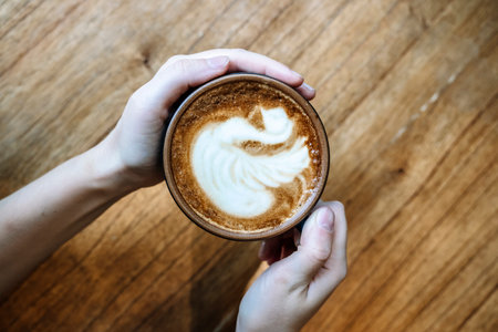 Cup of cappuccino in hand. Cup with hot coffee drink on the background of coffeeshop table.の写真素材