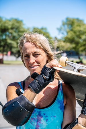 Smiling middle age woman portrait with skateboard in sport lifestyle at summer sunny day. Street urban sporty lifestyle concept.の写真素材