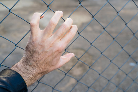 Hand on a metal fence. Border, prison, illegal migration concept.の写真素材