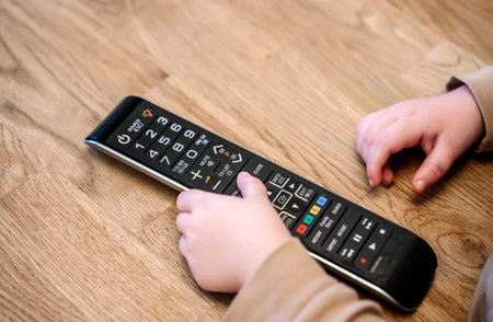 Child is watching TV. A child with a TV remote control in front of the screen.