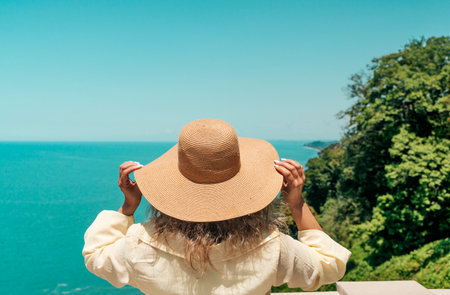 Woman in Summer Hat Looking at Sea Horizon from Cliffの写真素材