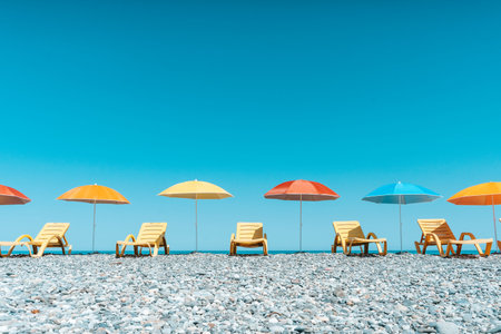 Colorful Beach Umbrellas and Sun Loungers on a Pebble Seaside