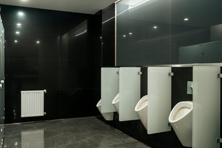 Modern Public Restroom Interior with White Urinals and Black Tiled Wallsの写真素材
