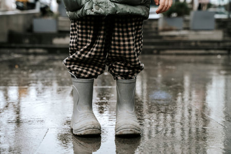 Toddler in Grey Rubber Boots and Plaid Pants on Wet Rainy Street