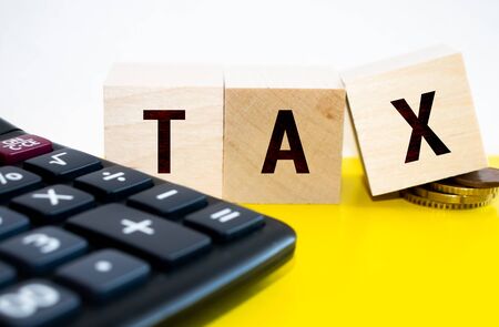 Close-up Of Person Hand Using Calculator With Tax Word On Wooden Blocksの写真素材