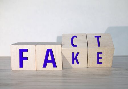 Business and design concept - surreal abstract geometric wooden cube take by hand with word " FACT & FAKE " concept on wood floor and white backgroundの写真素材