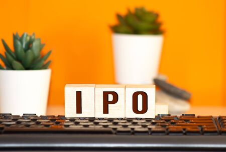 IPO Initial Public Offering written on a wooden cube in front of a laptopの写真素材
