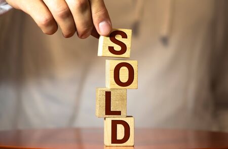realtor's hand puts a cube with a picture of the house to the word sold. Concept of selling a house, apartment, real estate. market of immobility. Trade of property. Affordable housing. Hand in suit.の写真素材
