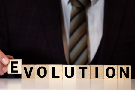 Close-up Of Persons Hand Placing Last Alphabet Of Word Evolve On Wooden Block