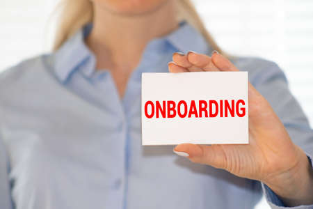 Person showing business card. Casual woman smiling holding the card. Shallow depth of field, focus on paper with ONBOARDING text.の写真素材