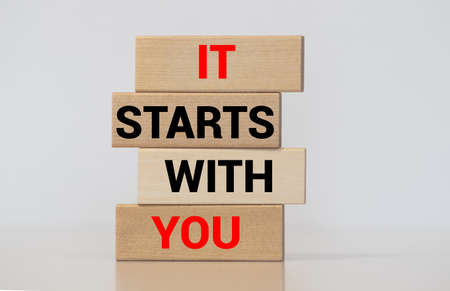 Male hand placing a block with word 'it' on top of a blocks tower with words 'starts with you'. Wooden table. Beautiful white background. Copy space.の写真素材