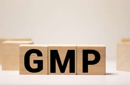 Good Manufacturing Practice. GMP the word on wooden cubes, cubes stand on a reflective surface, in the background is a business diagram. Business and finance conceptの写真素材