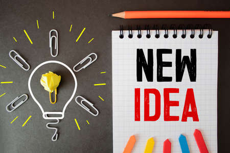 On the table there are reports of multi-colored charts, a magnifying glass and a sheet of paper in a black frame with the text NEW IDEA. Business conceptの写真素材