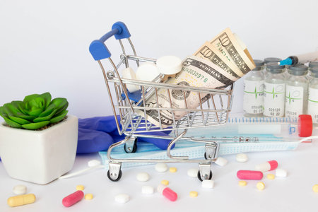 Shopping trolley with American and European banknotes and medical syringes and pills. On a blue...