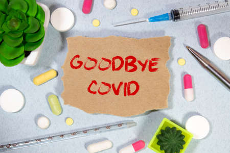 On a light blue background a card with the tex. GOODBYE CORONAVIRUS near the white bottle pills.の写真素材