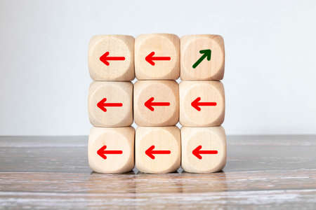 One of arrow move to opposite direction with others arrow which carved on wooden block cubes for business disruption and different thinking idea.の写真素材