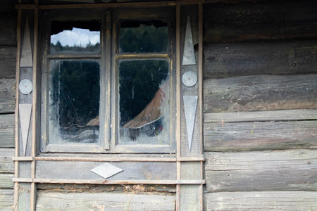 The facade of an old wooden log building with a small window divided into 4 parts and inside you can see a cup placed on a table.の写真素材