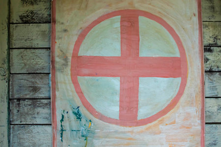 Red cross of the hospital, on the brick wall of the building, In a gray frame of stuccoed brickの写真素材